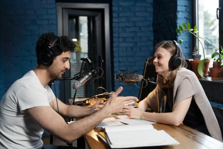 Man and woman recording a podcast together in a professional studio using microphones and headphones