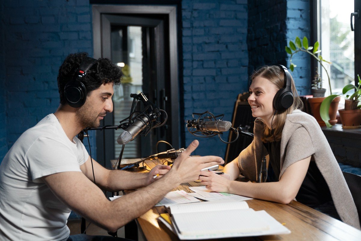 Man and woman recording a podcast together in a professional studio using microphones and headphones